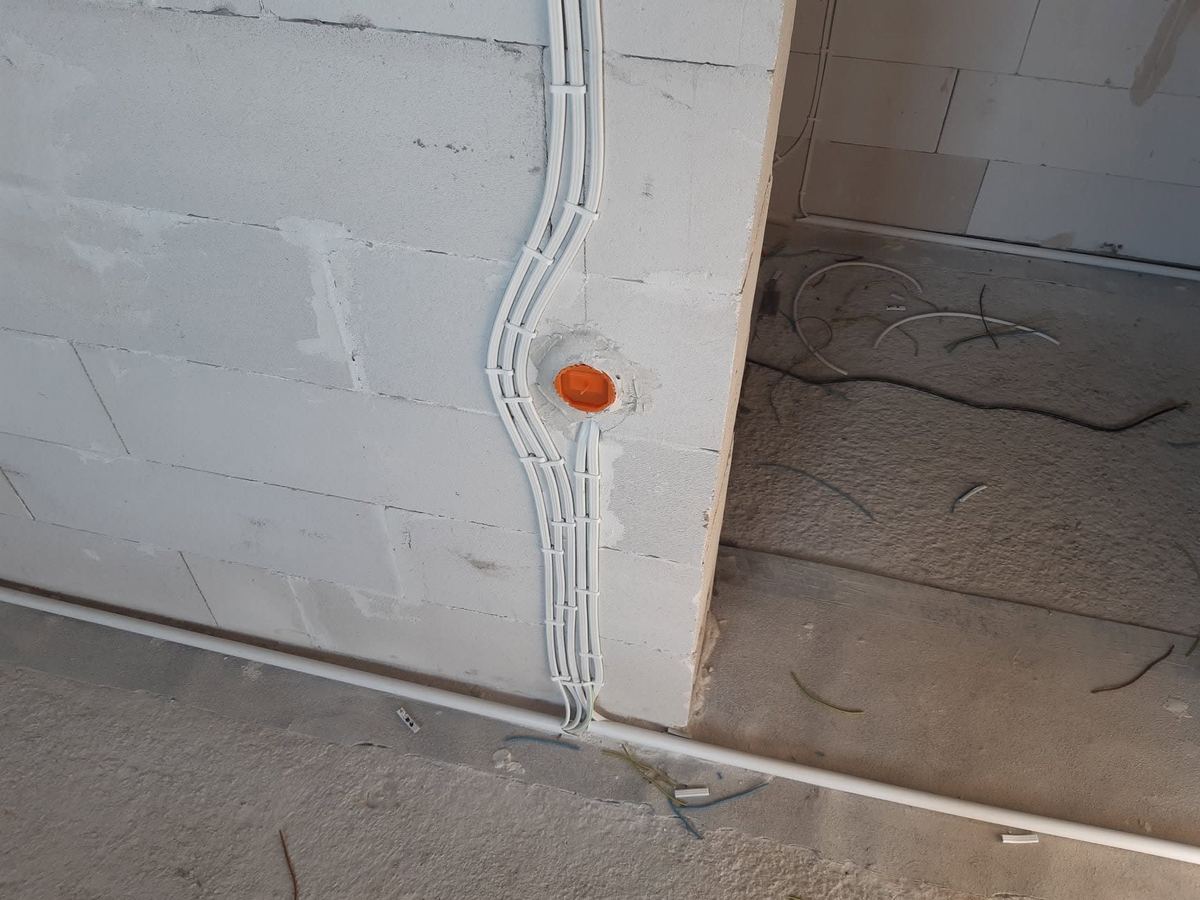 Przewody instalacji elektrycznej w rurkach karbowanych, równo poprowadzone i przypięte do ściany w domu w stanie surowym